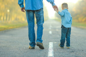 Un père marche main dans la main avec son enfant sur une route