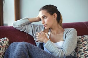 Jeune femme déprimée pensant à ses problèmes en buvant un café sur un canapé