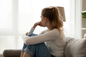Vue latérale d'une jeune femme regardant la fenêtre assise sur un canapé à la maison.